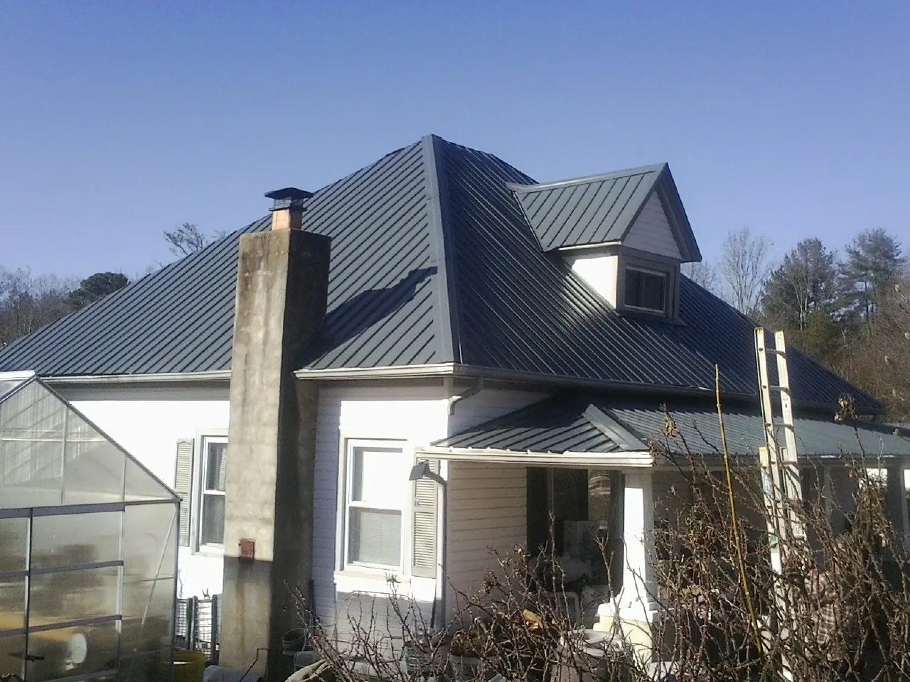 Dark blue standing seam metal roof on a white farmhouse with dormer — Slate & Tile Roof Repair by Roofing Brothers in Morganton