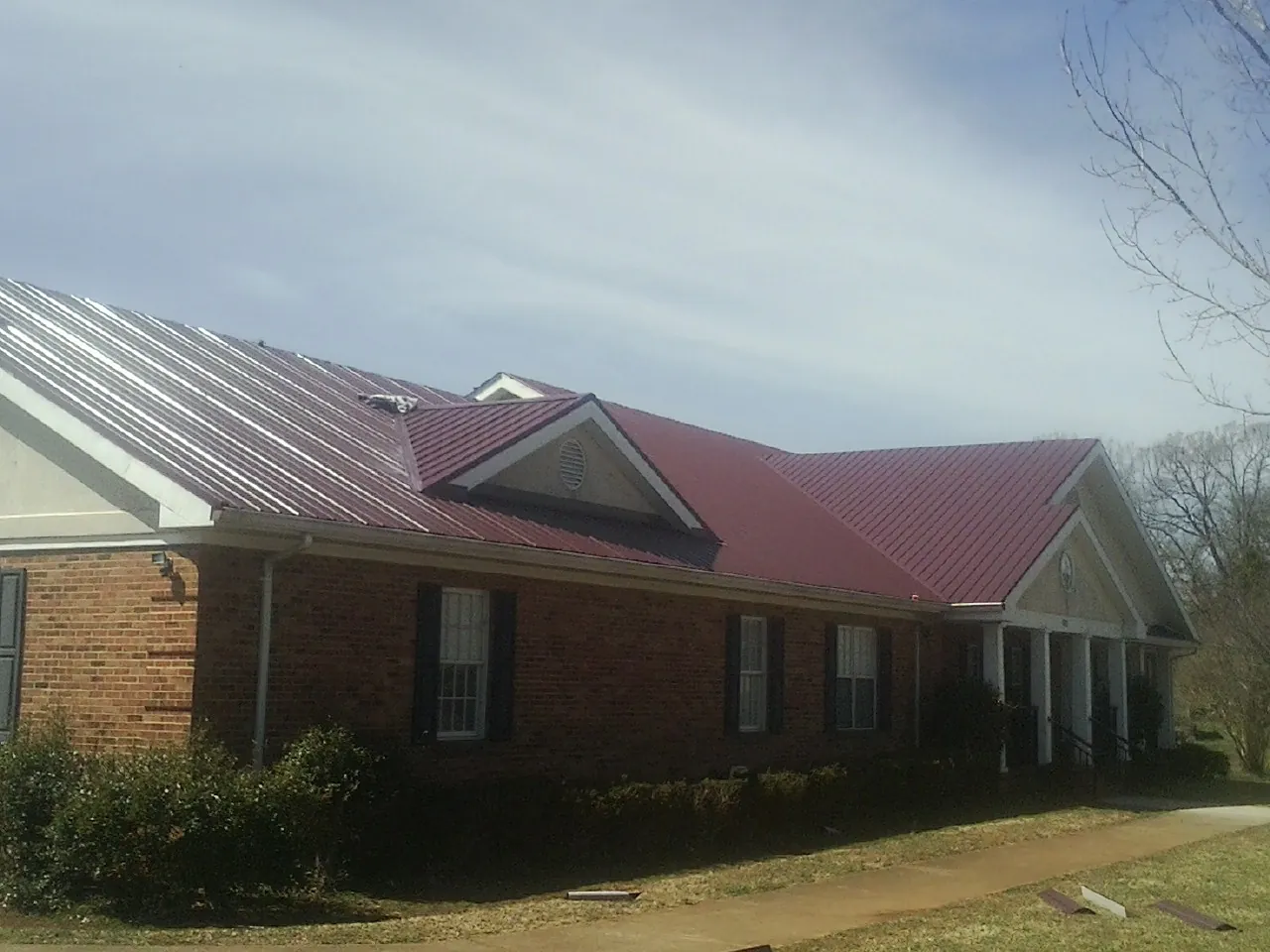 Red metal roof with gabled entries on a long brick building, from a Hail Damage Roof Repair job in Morganton