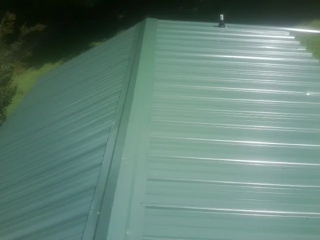 New green metal panels meeting at the ridge of a roof — Flat Roof Repair work by our crew in Morganton
