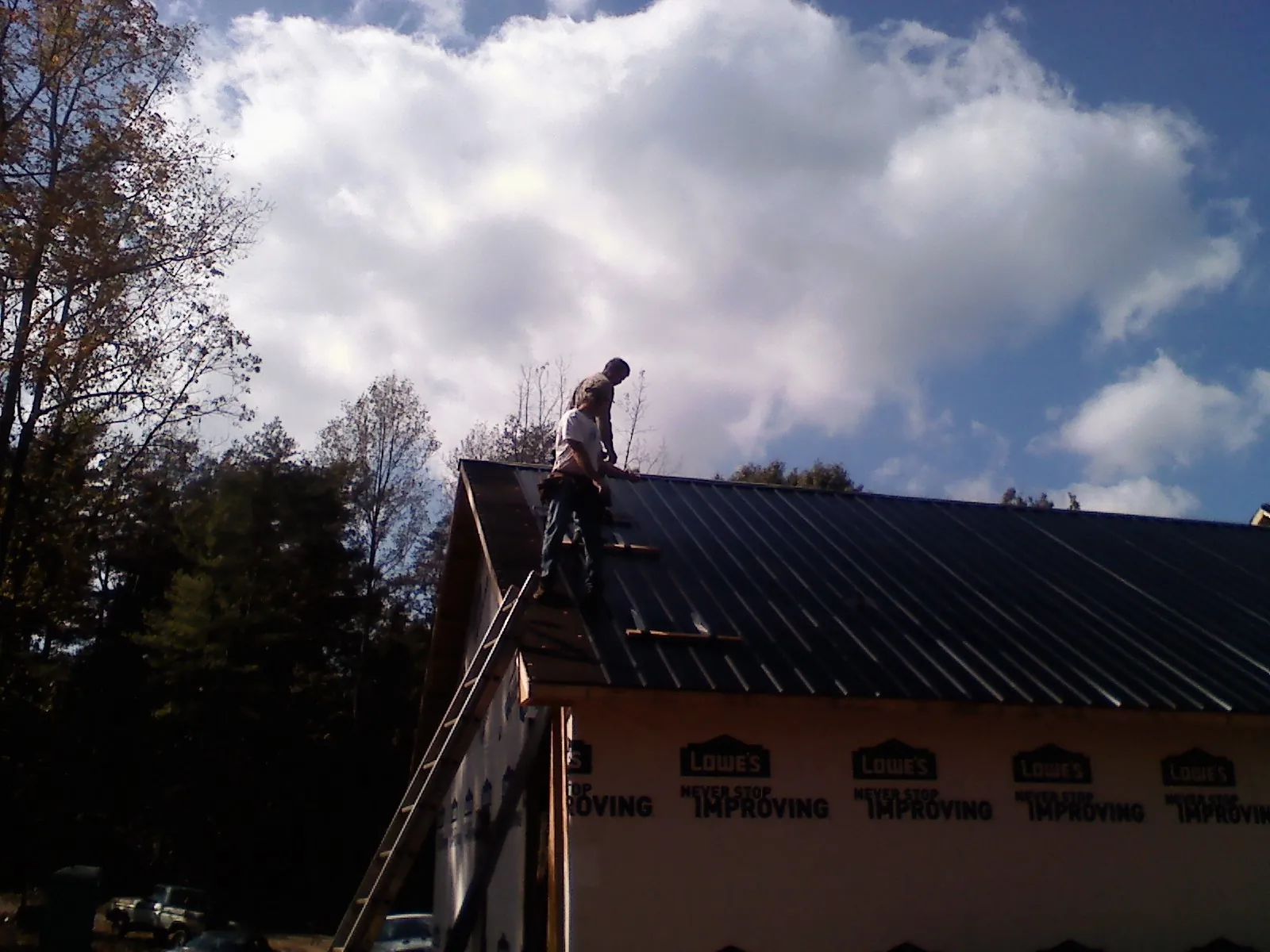 Roofer fastening dark metal panels high against a cloudy sky, from a Roof Inspection job in Morganton