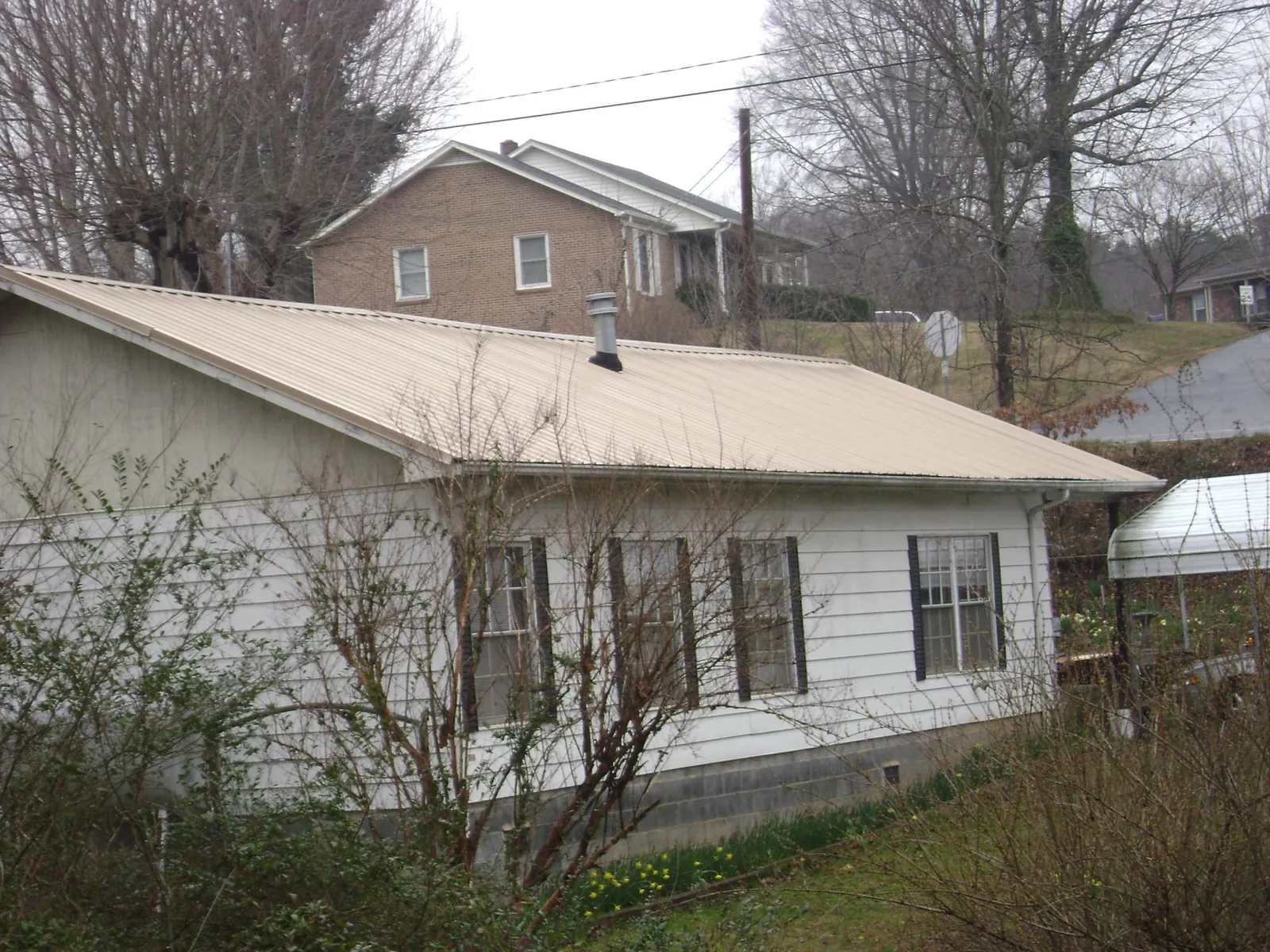 Tan metal roof on a white sided house set into a hillside — Commercial Roofing by Roofing Brothers in Morganton