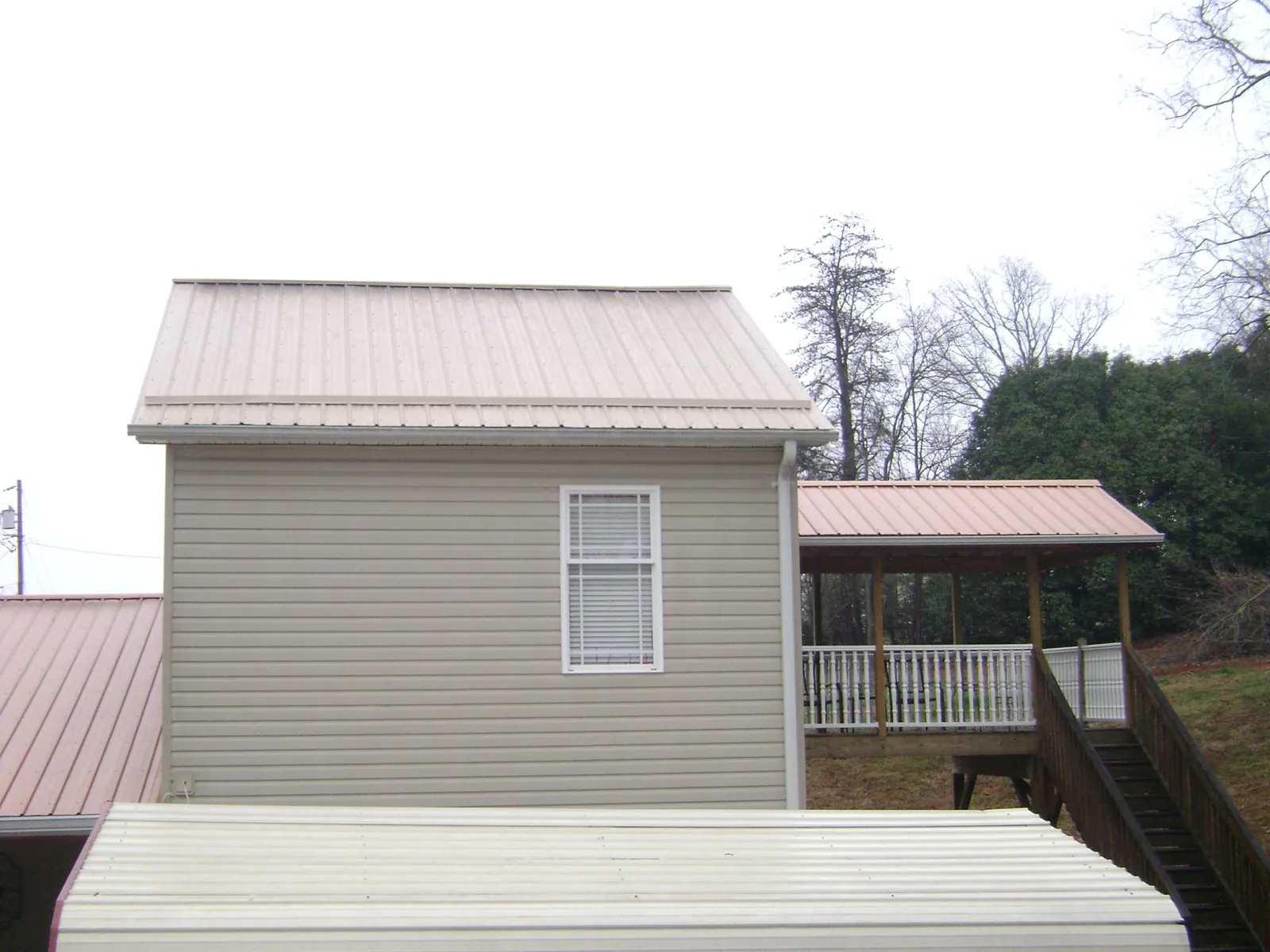 Tan metal roofs on a two story addition and attached porch, from a Roof Replacement job in Morganton